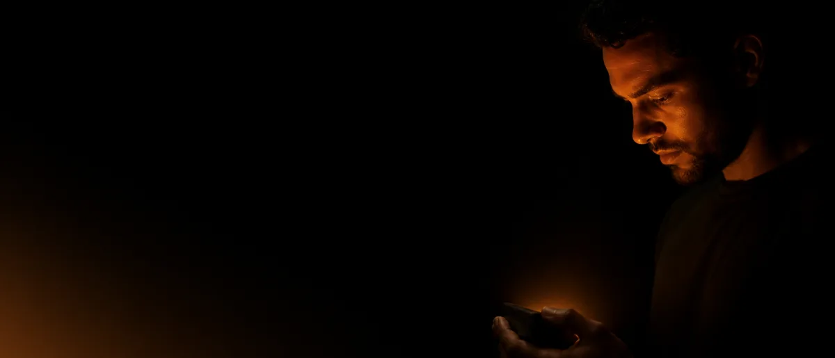 Rosto de perfil iluminado de baixo pela luz âmbar de um aparelho que a pessoa segura, contra fundo preto