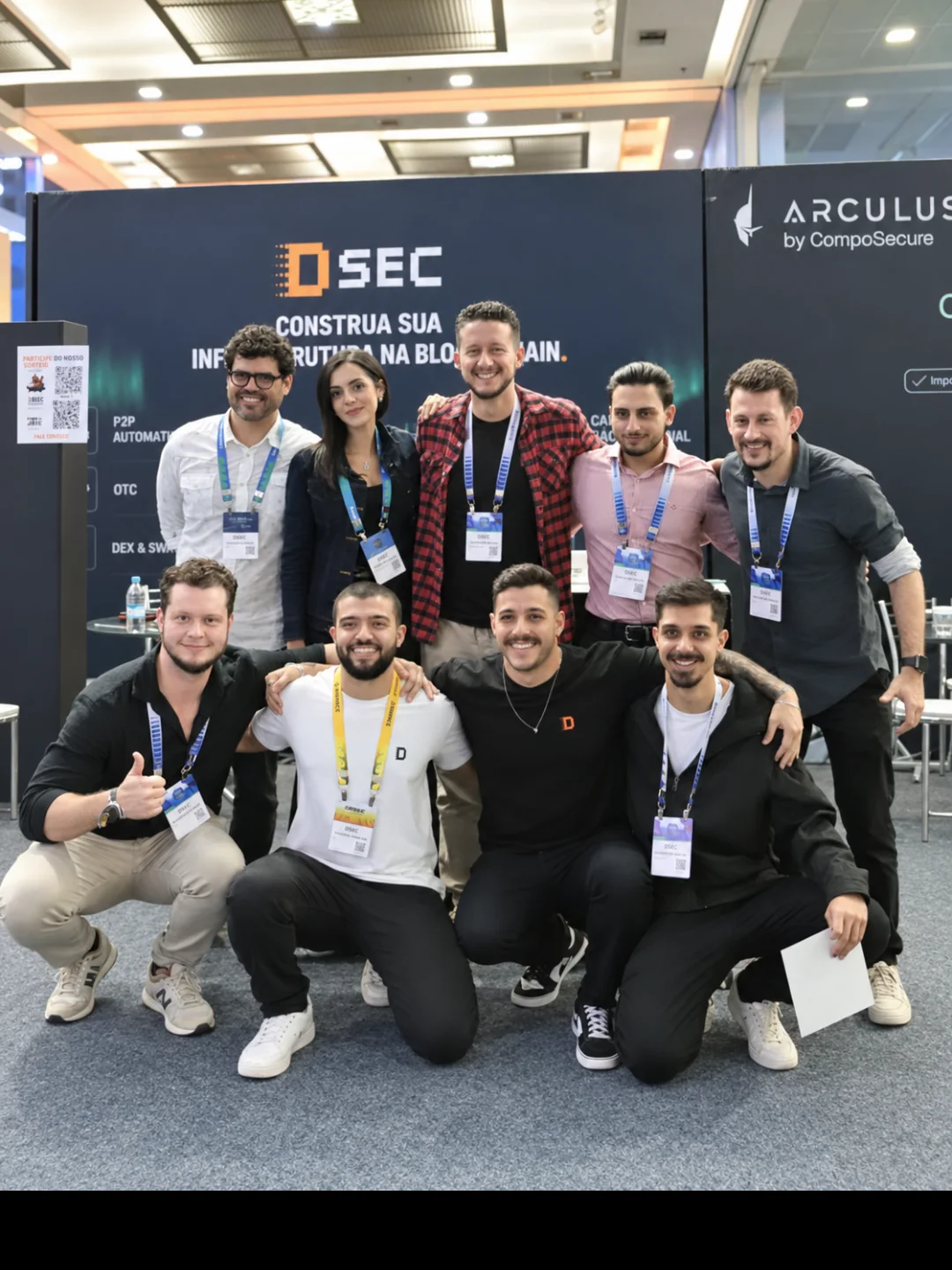 Nove integrantes da DSEC posando no estande próprio da empresa na Blockchain.RIO