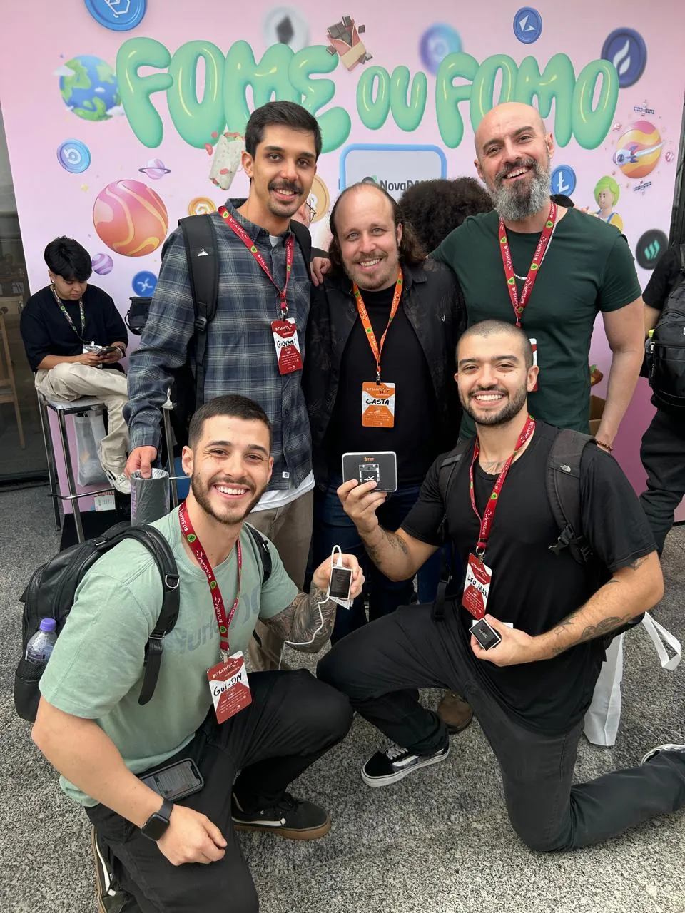Cinco pessoas posando diante do painel do evento Fome ou FOMO, com crachas no pescoço