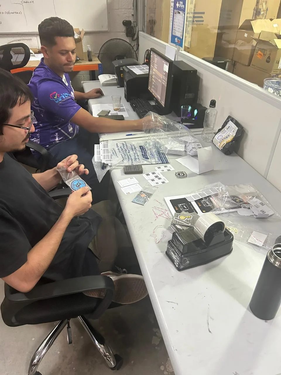 Duas pessoas montando kits sobre uma bancada, com embalagens e etiquetas espalhadas