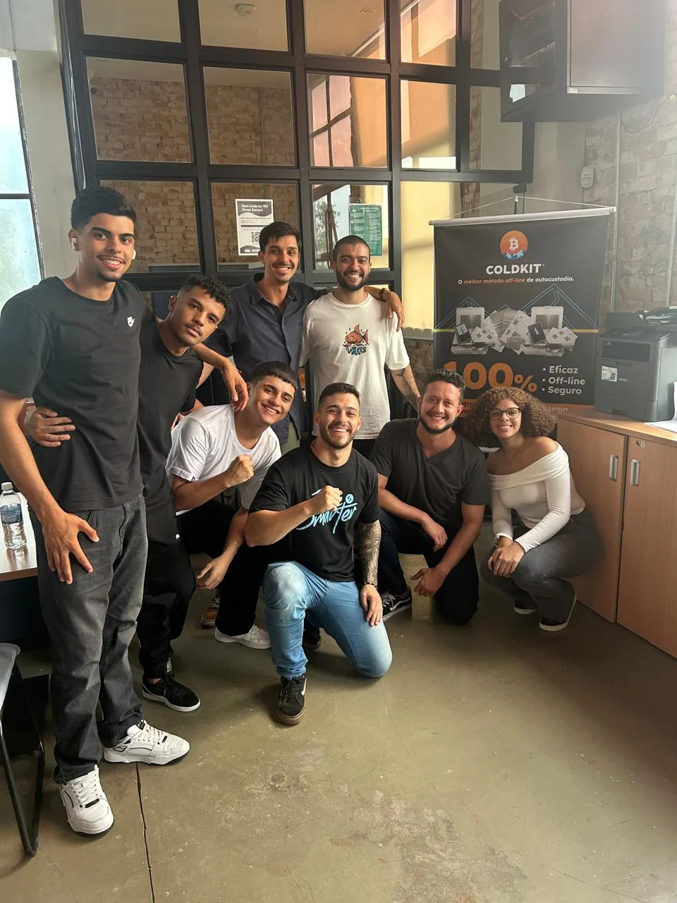 O time da DSEC reunido no escritório, ao lado de um banner do COLDKIT