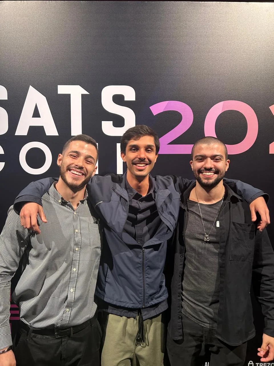 Tres integrantes da DSEC posando diante do painel da SATS Conf