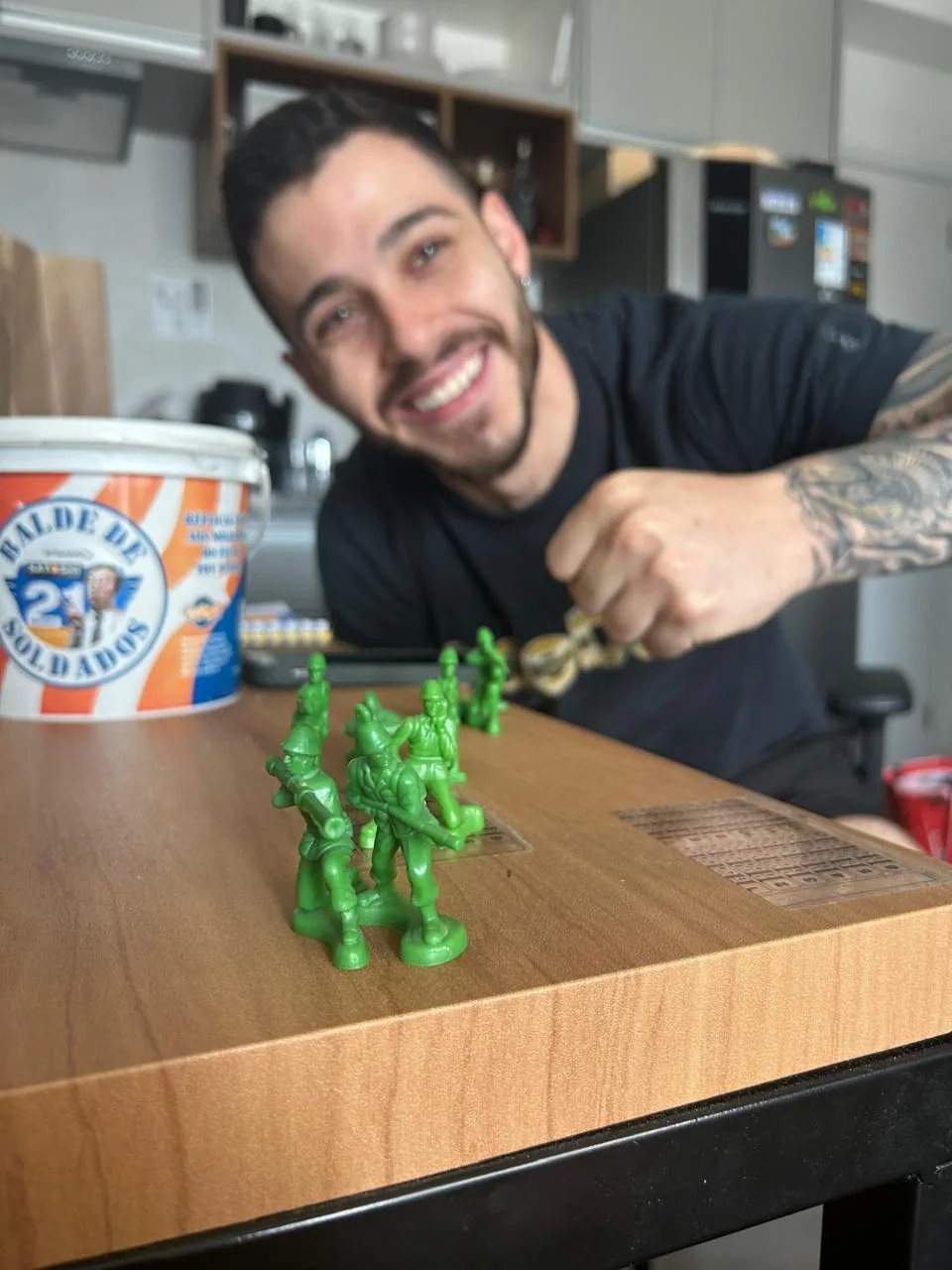 Homem sorrindo atras de uma mesa com soldadinhos de chumbo verdes enfileirados
